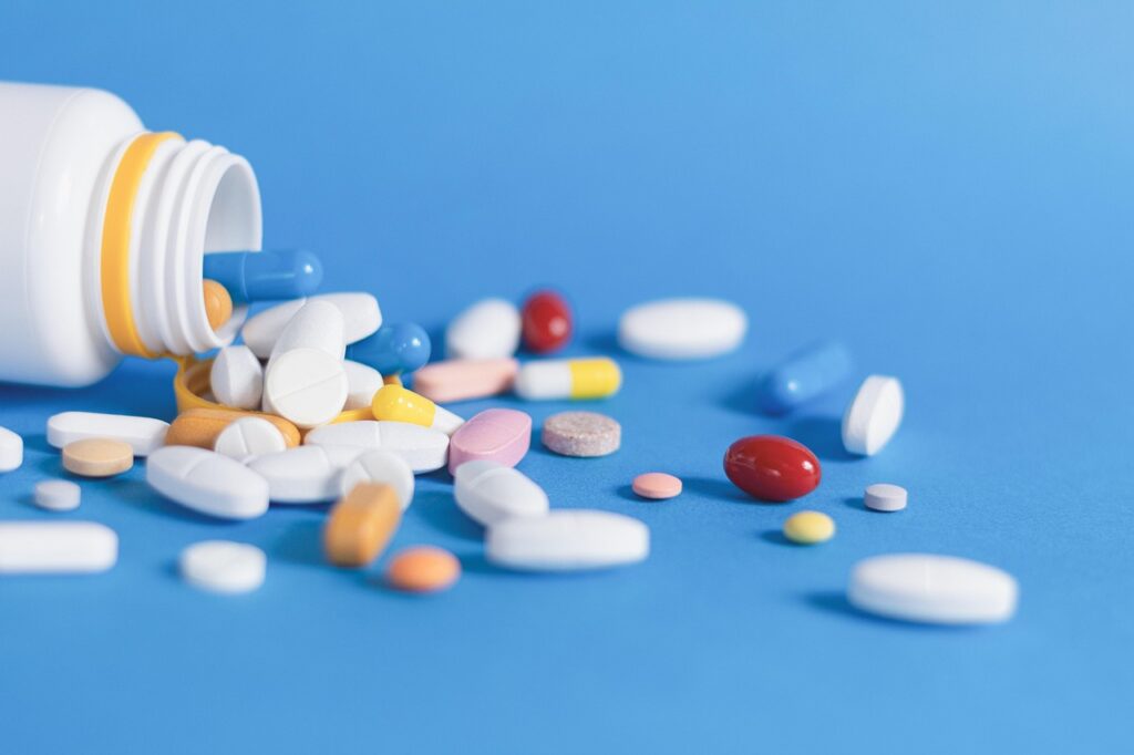 Spilled prescription pill bottle with assorted tablets and capsules on a blue background, representing medication management and polypharmacy concerns for seniors.