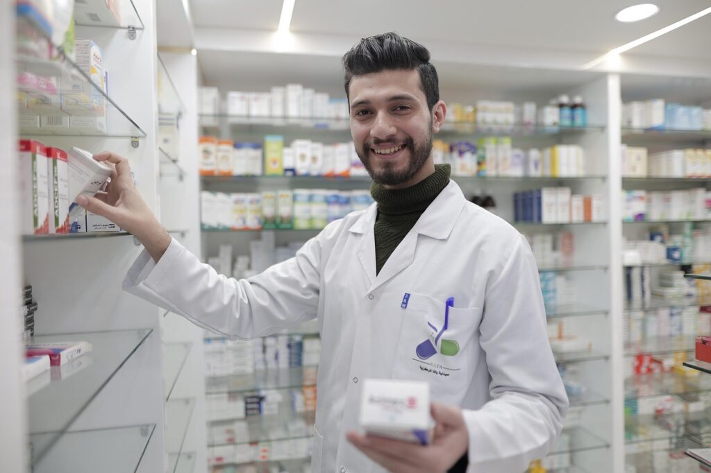 Pharmacist in a white lab coat standing in a pharmacy, selecting a medication from a shelf and holding a prescription box, representing professional medication management review.